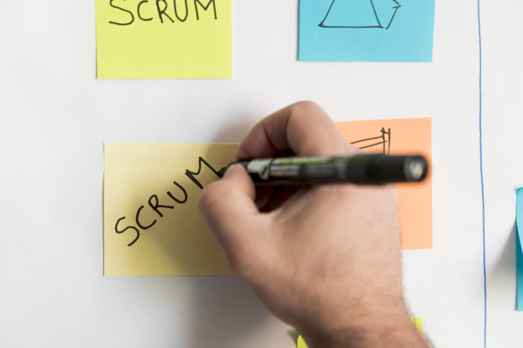 A person writing scrum on a post it